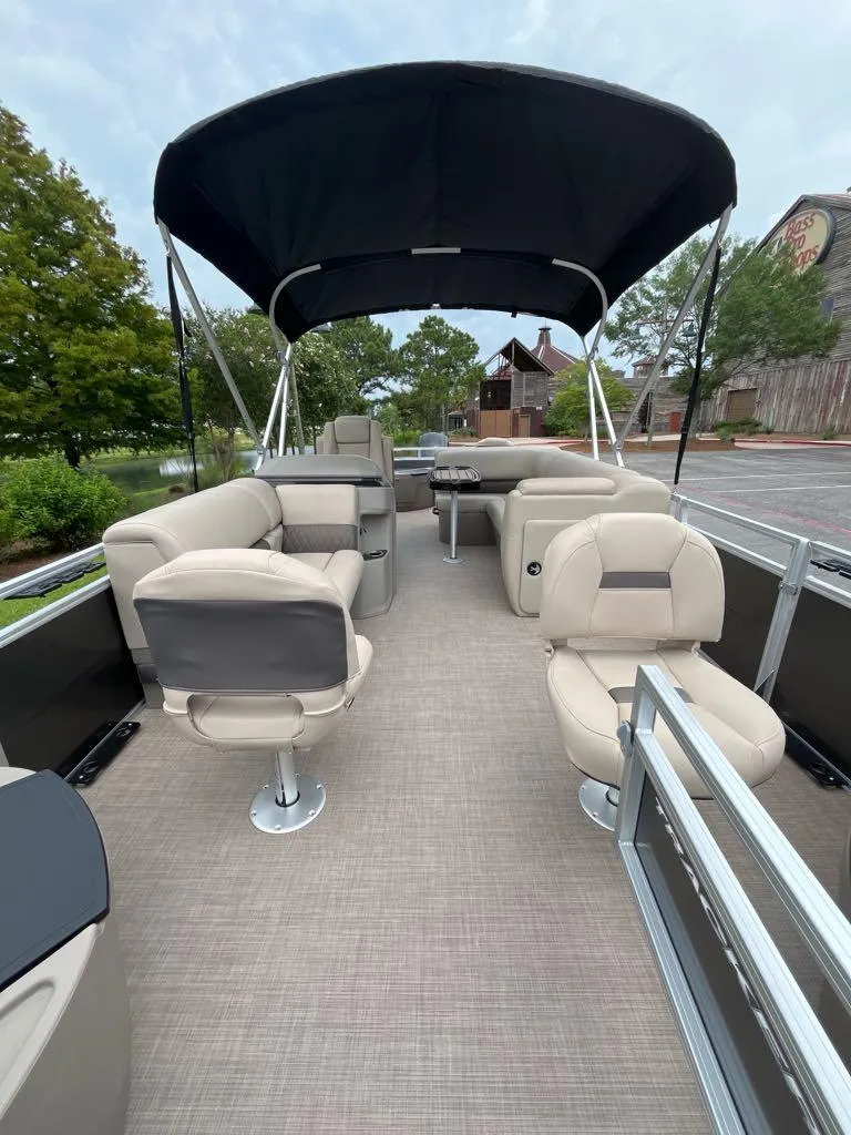 Slide: The Image of 2025 Sun Tracker Fishin' Barge 20 DLX interior with seating and canopy, parked outdoors. - 2