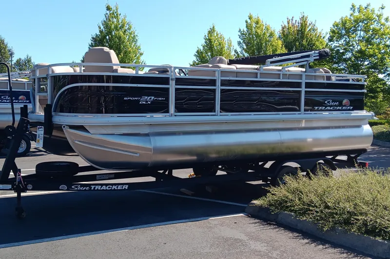 The Image of 2025 Sun Tracker SportFish 20 DLX pontoon boat on trailer in parking lot. - 0