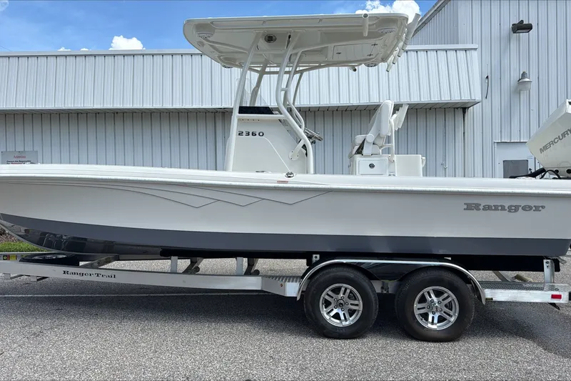 Slide: The Image of 2025 Ranger 2360 Bay boat on trailer, parked outside a metal building. - 0