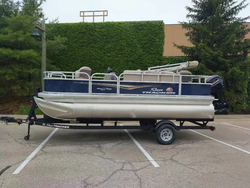 The Image of 2025 Sun Tracker Bass Buggy 18 DLX pontoon boat on trailer in parking lot. - 0