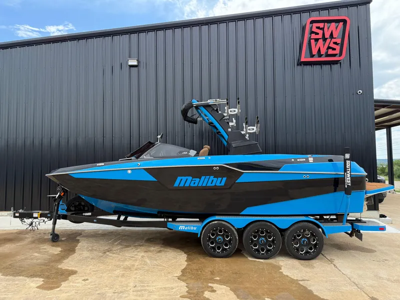 The Image of 2021 Malibu M240 boat in blue and black, parked on a trailer outside a building. - 0