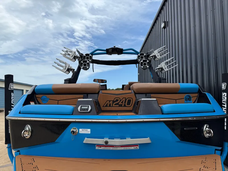 Slide: The Image of 2021 Malibu M240 boat with blue and brown seating, docked near a metal building. - 15