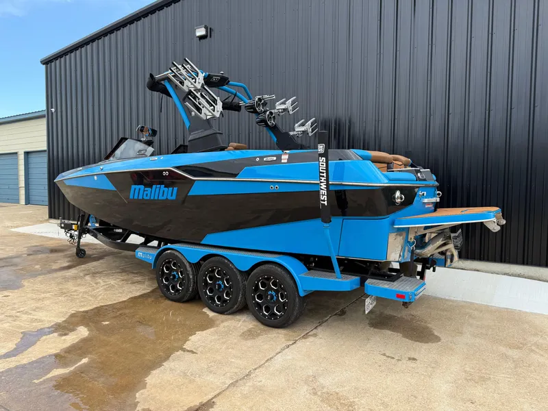 Slide: The Image of 2021 Malibu M240 boat in blue and black, parked on a trailer near a building. - 3