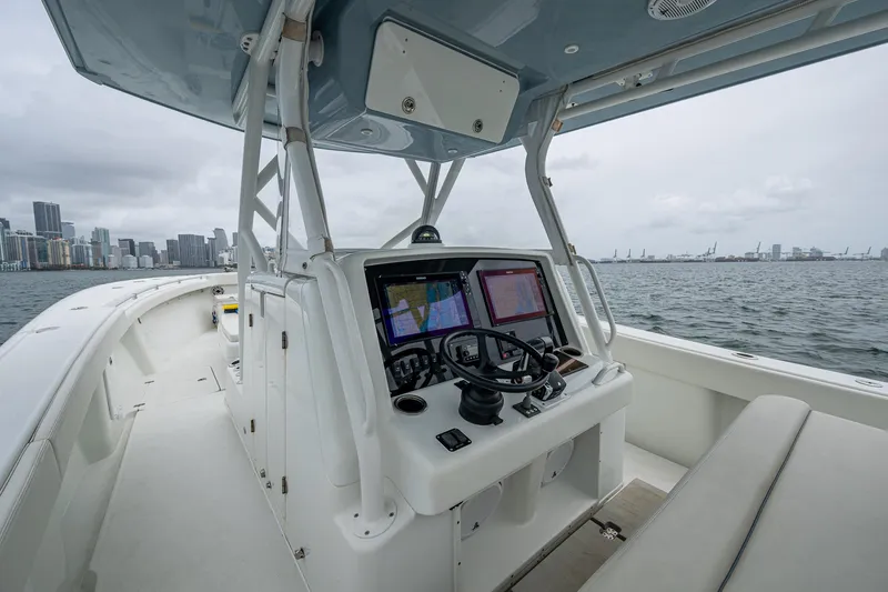 Slide: The Image of 2013 Yellowfin 39 Offshore boat cockpit with navigation screens, steering wheel, and city skyline in background. - 46
