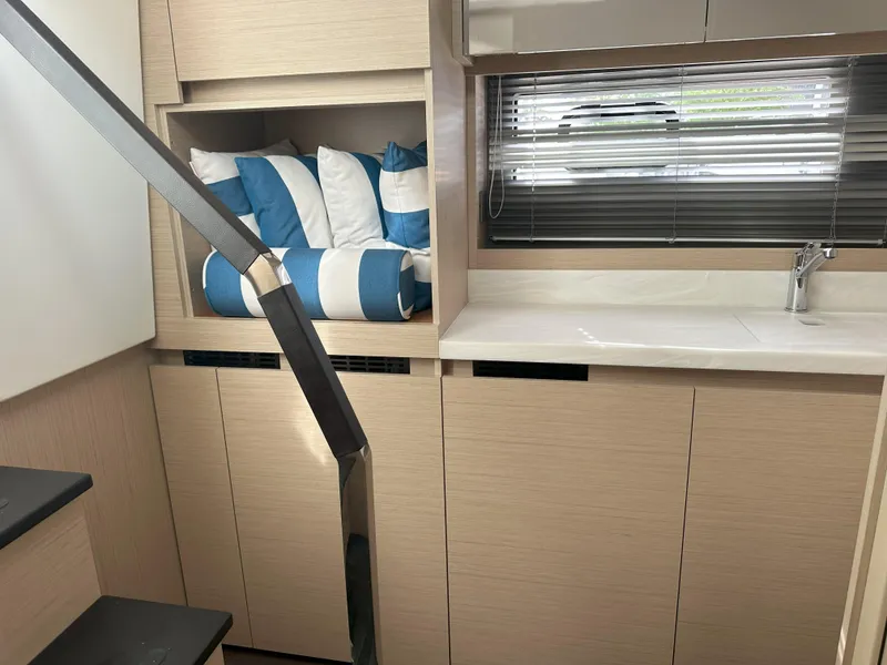 Slide: The Image of 2024 Jeanneau DB 43 interior with modern cabinetry, striped cushions, and sleek sink area. - 27