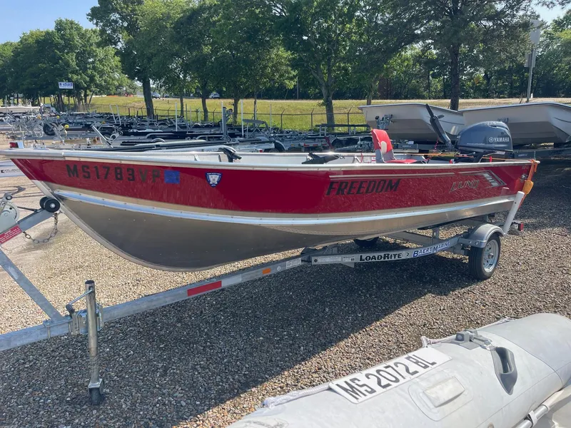 Slide: The Image of 2025 Lund SSV-16 Tiller boat on trailer, red and silver, parked outdoors. - 2