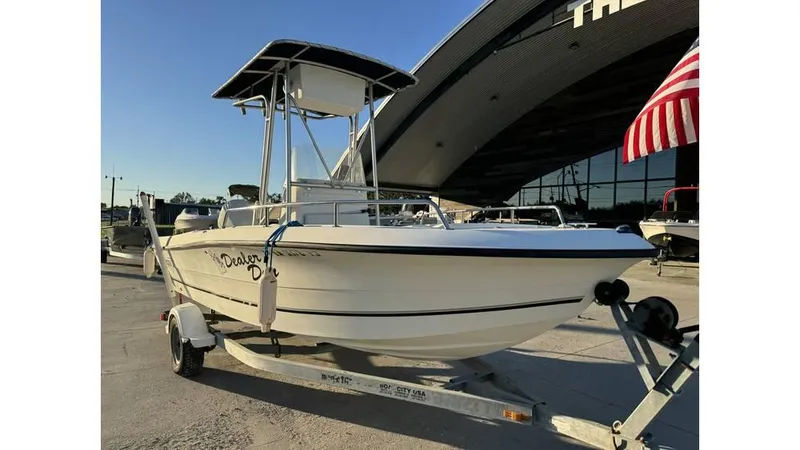 The Image of 2004 Sea Boss 190 Center Console boat on trailer, parked near a building with an American flag. - 1