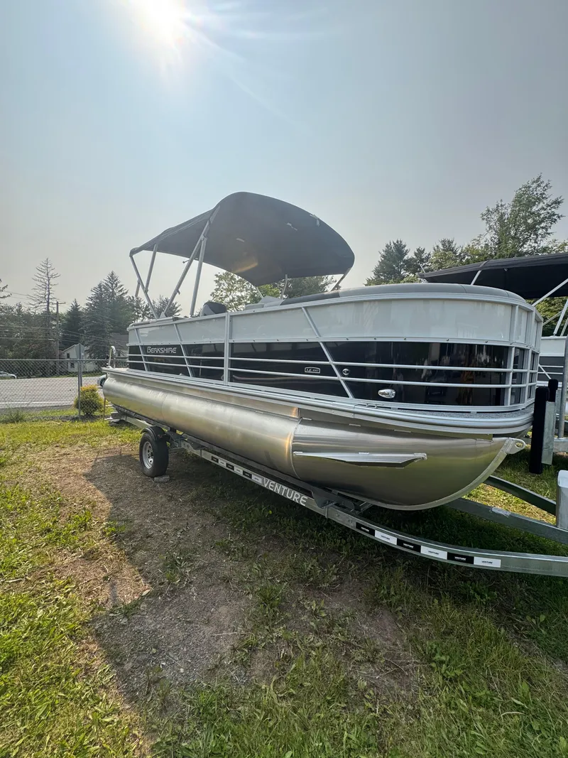 The Image of 2025 Berkshire 22RFX LE pontoon boat with canopy on trailer, parked on grass. - 0