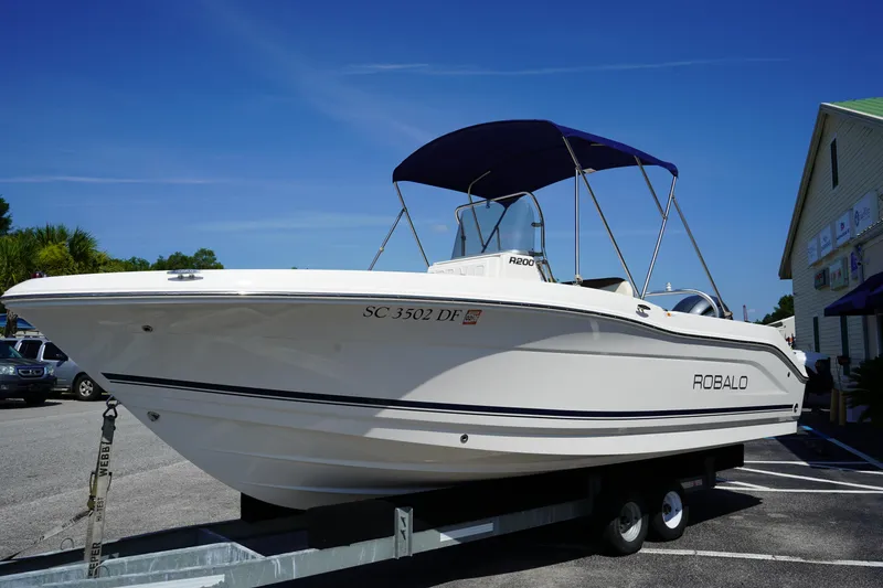 Slide: The Image of 2017 Robalo R200ES boat on trailer with blue canopy, parked outdoors. - 2