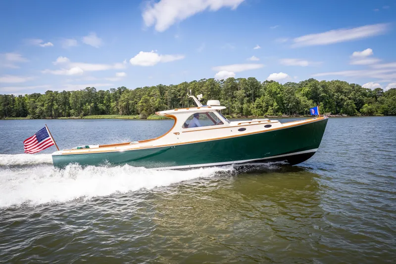 Slide: The Image of Hinckley Picnic Boat Classic 1997 cruising on a lake with American flag, clear sky, and forest backdrop. - 16