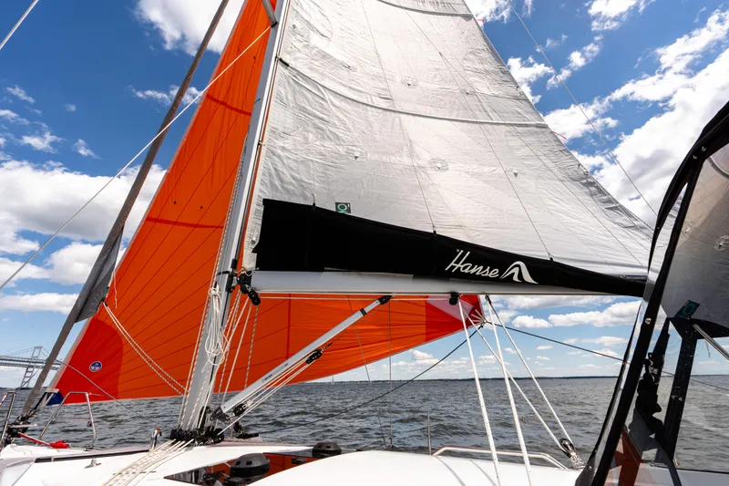 Slide: The Image of 2023 Hanse 348 sailboat with vibrant orange sails on open water under blue sky. - 20
