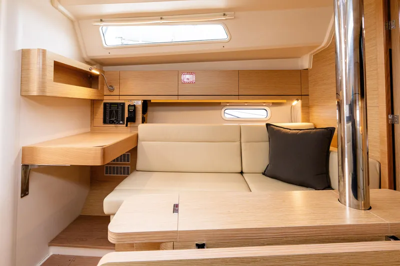 Slide: The Image of 2023 Hanse 348 yacht interior with beige seating, wooden accents, and a small window. - 40