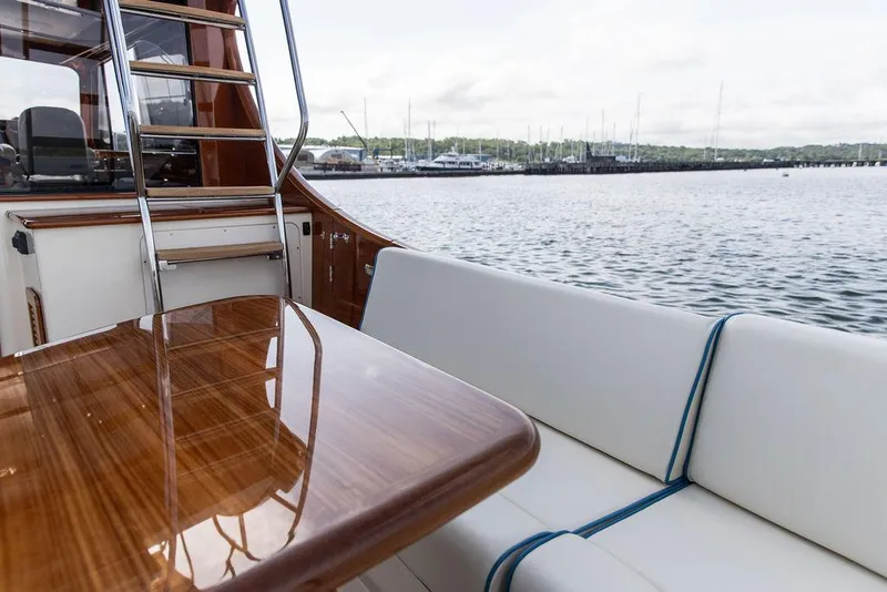 Slide: The Image of 2017 Hinckley Talaria 43 Flybridge yacht with elegant seating and polished wood table by the water. - 7