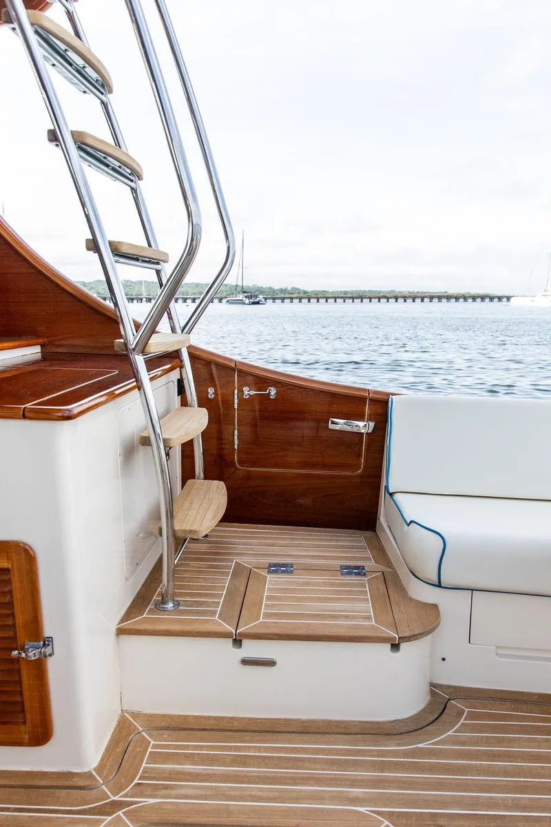 Slide: The Image of Hinckley Talaria 43 Flybridge 2017, elegant wooden interior, ladder, and seating area by the water. - 8
