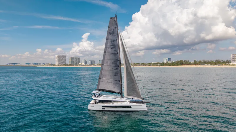 Slide: The Image of 2019 McConaghy MC60 sailing near a coastal city under a partly cloudy sky. - 5