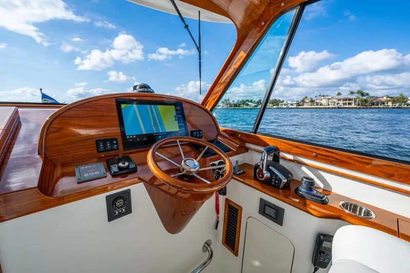 Slide: The Image of 2024 Hinckley 35 boat cockpit with wooden steering wheel and navigation system, overlooking serene waters. - 16