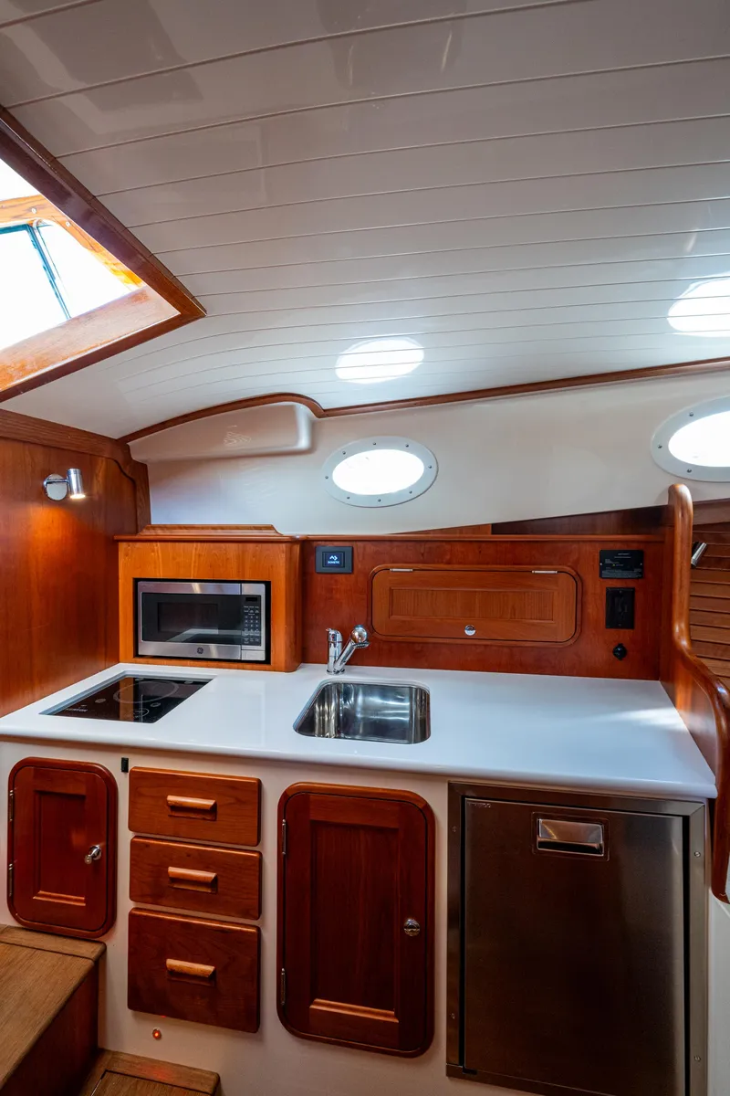 Slide: The Image of 2024 Hinckley 35 yacht interior kitchen with wooden cabinetry, sink, stove, and microwave. - 20