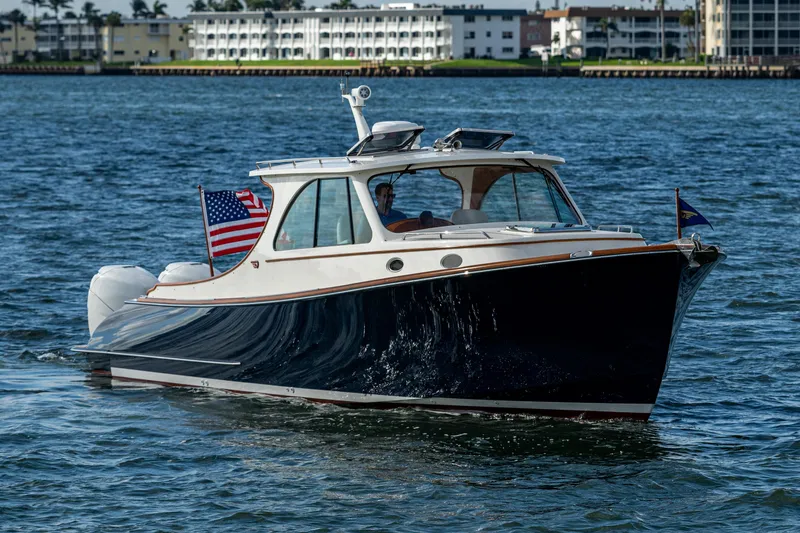 Slide: The Image of 2024 Hinckley 35 boat cruising on water with American flag, coastal buildings in background. - 2