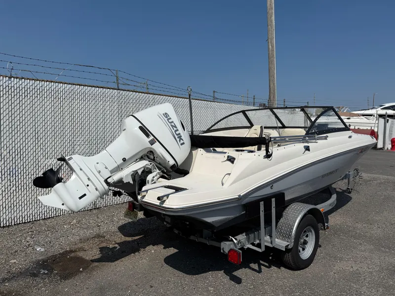 Slide: The Image of 2023 Stingray 191 DC boat with Suzuki outboard motor on trailer, parked outdoors. - 2