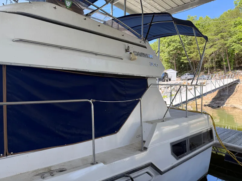 Slide: The Image of 1994 Carver 300 boat docked with blue canopy and railing, surrounded by trees. - 2
