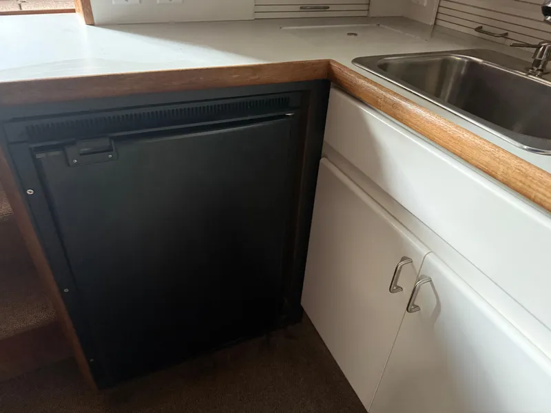 Slide: The Image of 1994 Carver 300 boat kitchen with black fridge, white cabinets, and stainless steel sink. - 29