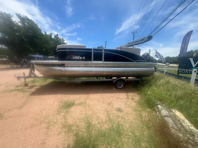 Slide: The Image of 2024 Harris FloteBote 210 Breeze pontoon boat parked on a trailer outdoors. - 2