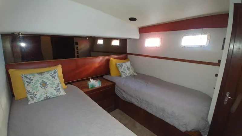 Slide: The Image of 1987 Hatteras 65 Convertible cabin with twin beds, decorative pillows, and small windows. - 36