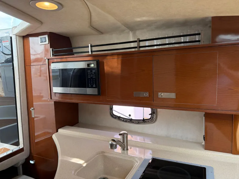Slide: The Image of 2009 Sea Ray 270 Sundancer interior kitchen with microwave, sink, and wooden cabinets. - 21