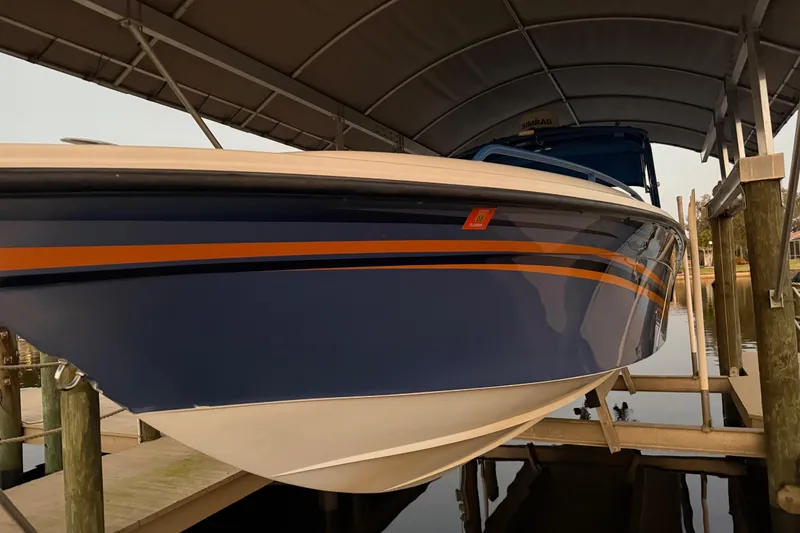 Slide: The Image of 2011 Spectre 360 Roadster boat docked under a canopy, featuring sleek blue and orange design. - 61