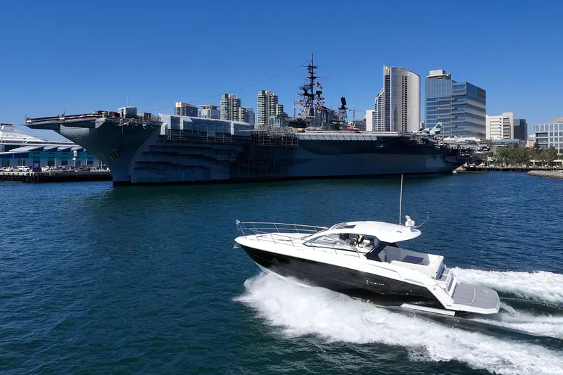 Slide: The Image of 2021 Cruisers Yachts 390 Express Coupe cruising near a large battleship in a city harbor. - 3