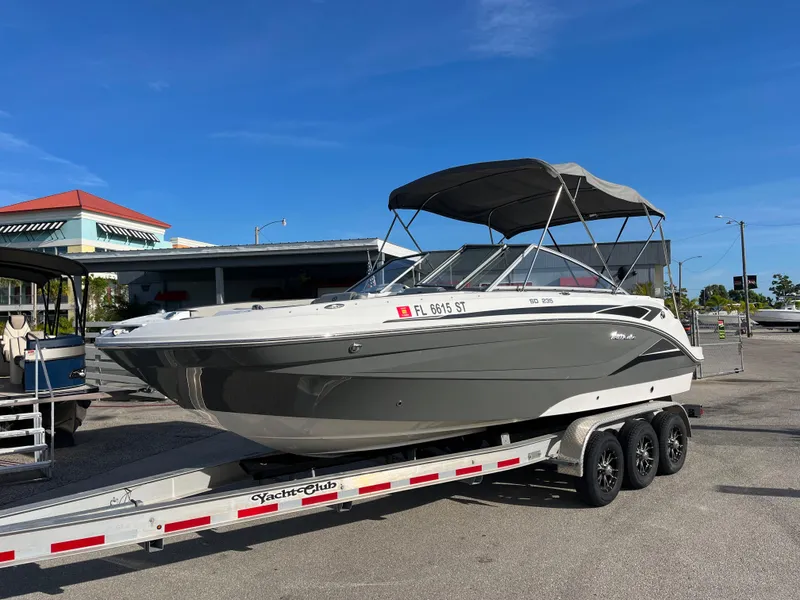 The Image of 2020 Hurricane SunDeck 235 OB boat on trailer, parked outdoors under clear blue sky. - 1