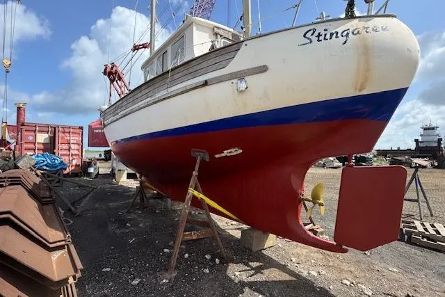 Slide: The Image of 1977 Fisher 37 MS sailboat on dry dock, red and white hull, named "Stingaree." - 2