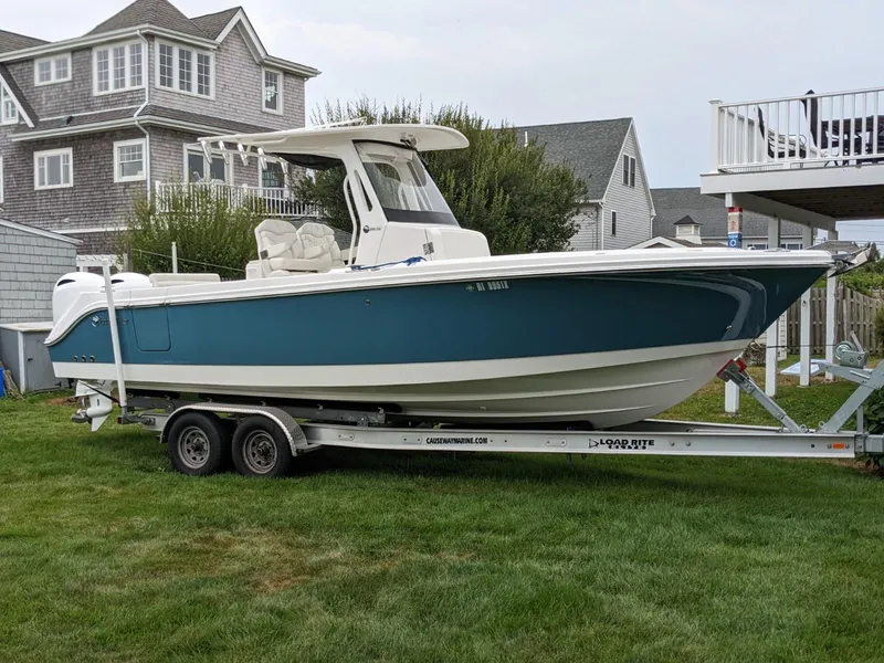The Image of 2021 Edgewater 262 CC boat on trailer, parked on grass near coastal homes. - 0