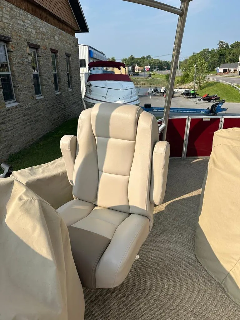Slide: The Image of 2017 Godfrey Sweetwater 2386 CC boat with beige captain's chair, docked near a stone building. - 10