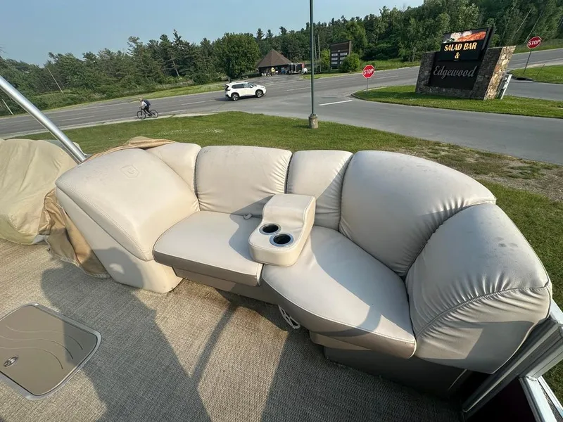 Slide: The Image of 2017 Godfrey Sweetwater 2386 CC boat with beige seating and cup holders, parked near a road. - 12