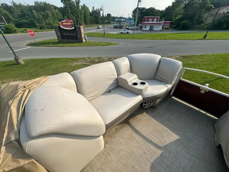 Slide: The Image of 2017 Godfrey Sweetwater 2386 CC boat with beige seating and cup holders, parked near a road. - 13