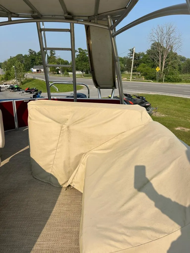 Slide: The Image of 2017 Godfrey Sweetwater 2386 CC boat with covered seating and ladder, parked near a road. - 18