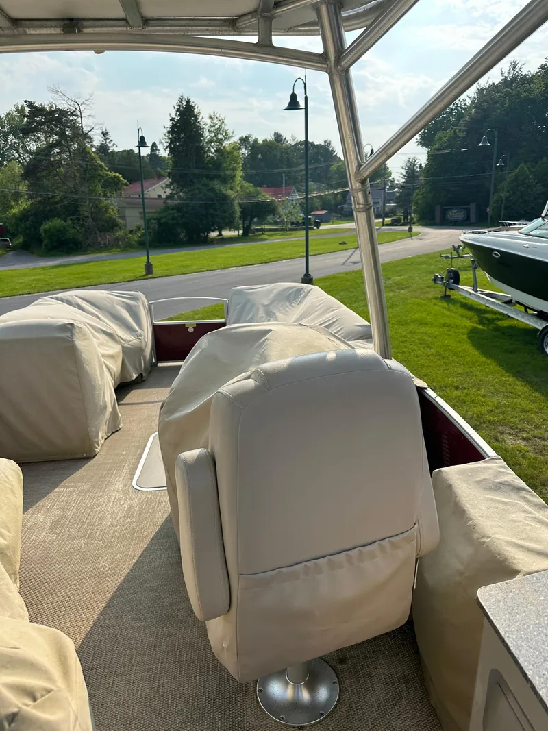 Slide: The Image of 2017 Godfrey Sweetwater 2386 CC boat interior with covered seats, parked on grass. - 19
