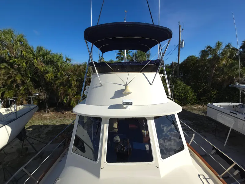 Slide: The Image of 2004 Legacy Sedan Flybridge boat with canopy, docked near lush greenery. - 16