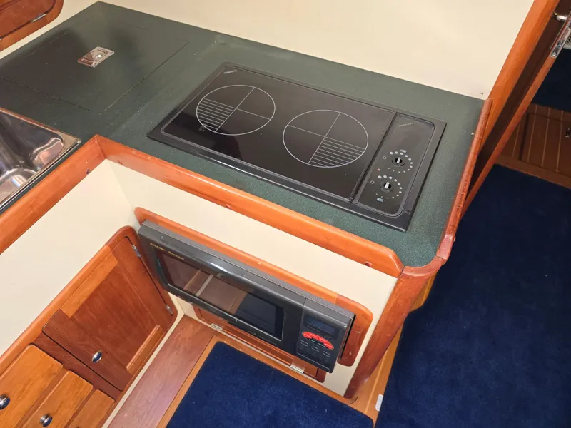 Slide: The Image of 2004 Legacy Sedan Flybridge kitchen with stove and microwave, featuring wood cabinetry and blue carpet. - 35