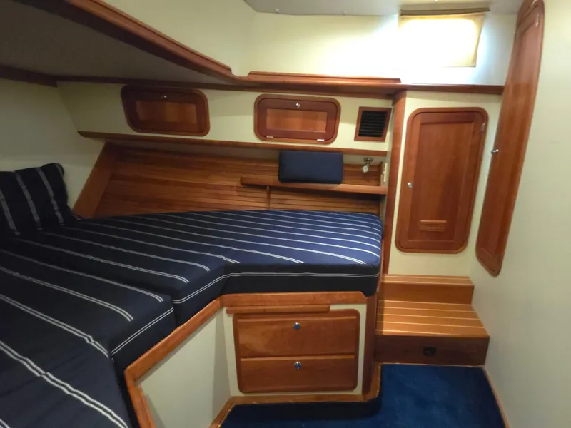 Slide: The Image of 2004 Legacy Sedan Flybridge cabin with striped bedding, wooden storage, and cozy interior design. - 45