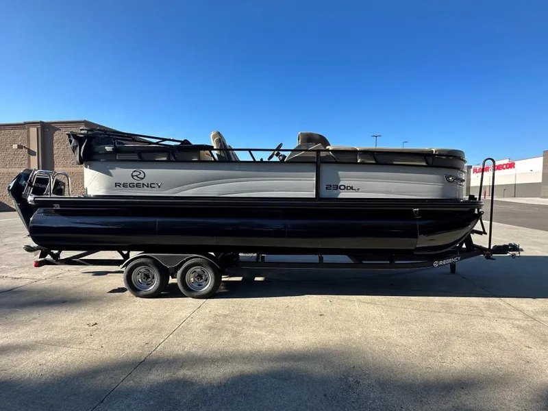 Slide: The Image of 2024 Regency 230 DL3 pontoon boat on trailer, parked outdoors under clear blue sky. - 1