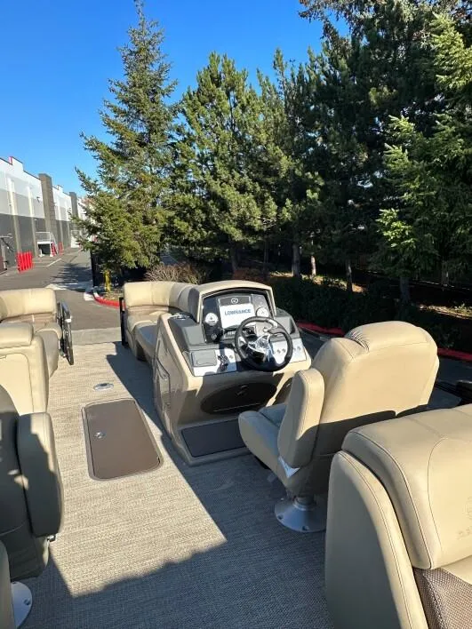 Slide: The Image of 2024 Regency 230 DL3 pontoon boat interior with beige seating and steering console. - 2