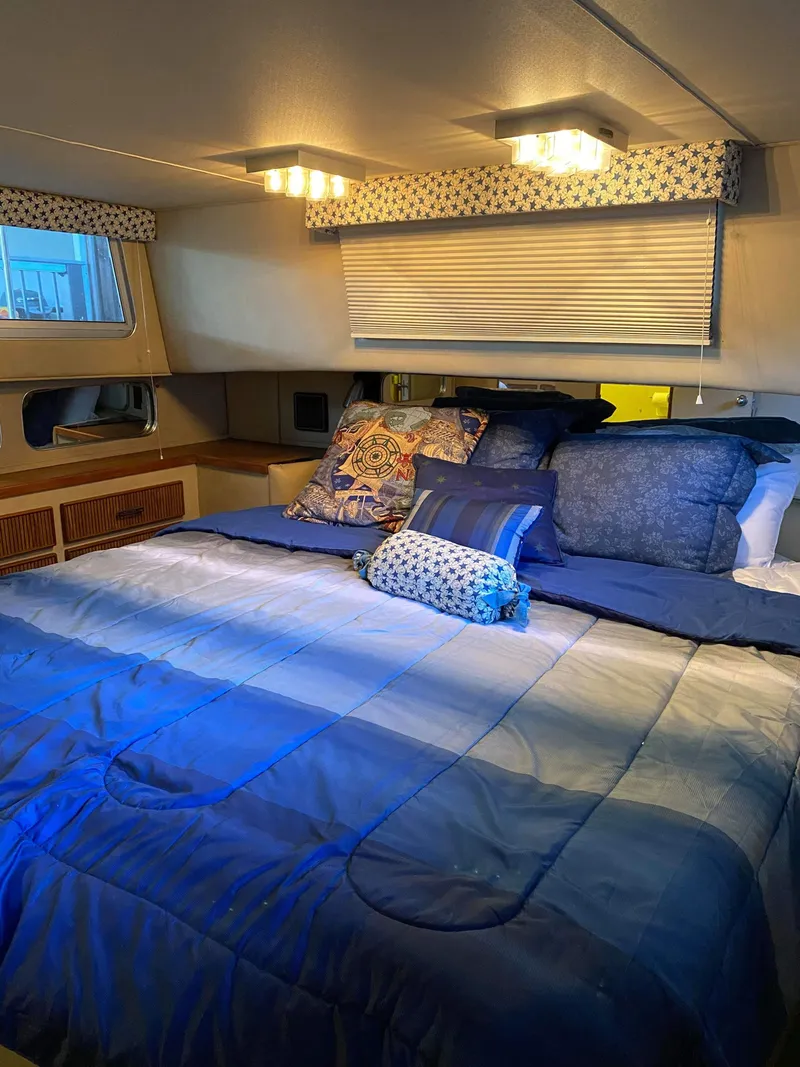 Slide: The Image of 1985 Chris-Craft 381 Catalina cabin with cozy bed, blue bedding, and ambient lighting. - 7