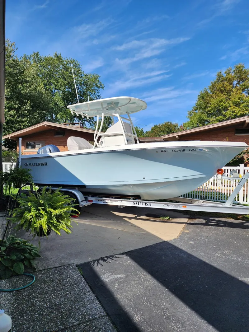 The Image of 2022 Sailfish 220 CC boat on trailer, parked in driveway, surrounded by greenery and blue sky. - 0