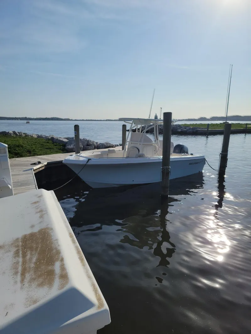 Slide: The Image of 2022 Sailfish 220 CC boat docked on calm water under clear sky. - 2