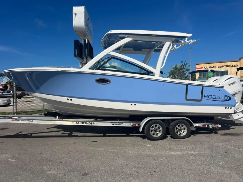 Slide: The Image of 2025 Robalo R257 Dual Console boat on trailer, blue and white design, parked outdoors. - 2