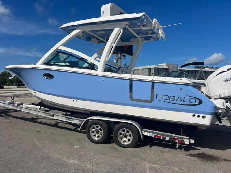 Slide: The Image of 2025 Robalo R257 Dual Console boat on trailer, blue and white design, parked outdoors. - 3