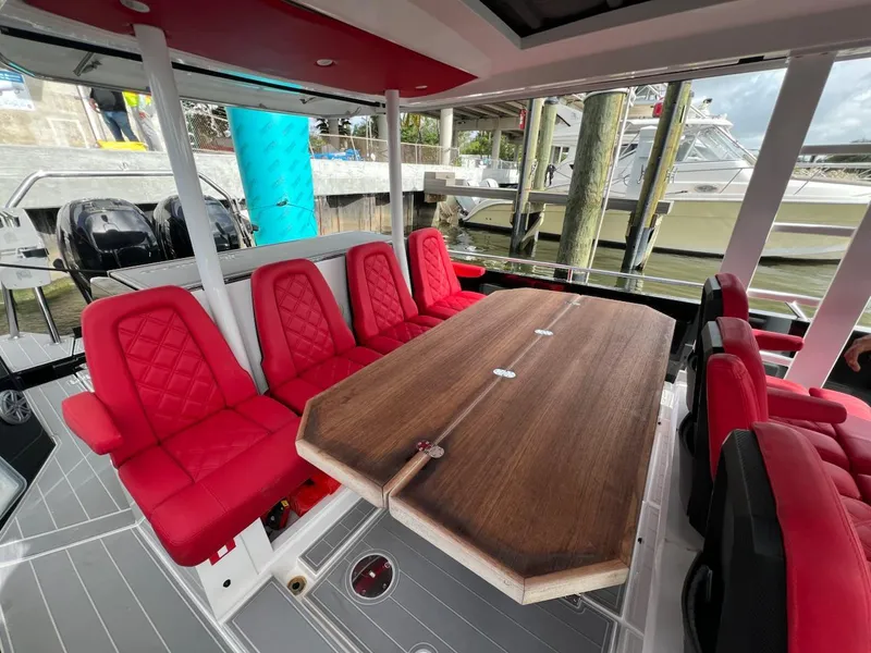 Slide: The Image of 2018 Axopar 37 Sun Top with red seating and wooden table in a marina setting. - 13