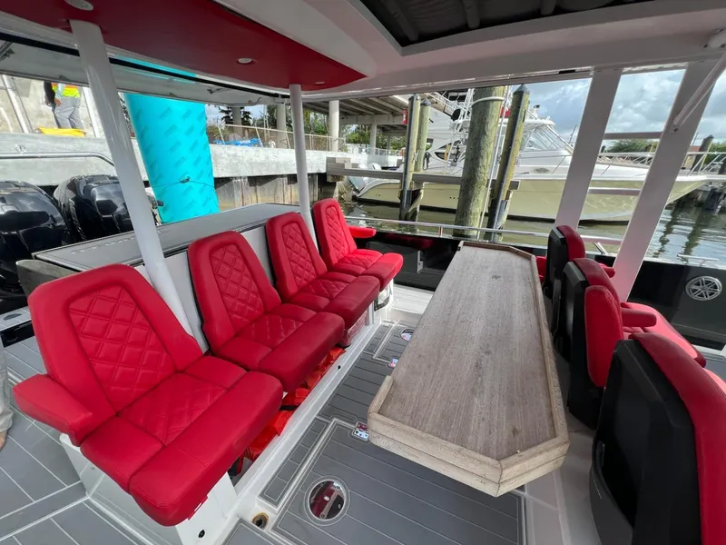 Slide: The Image of 2018 Axopar 37 Sun Top with red seating and a wooden table, docked at a marina. - 16